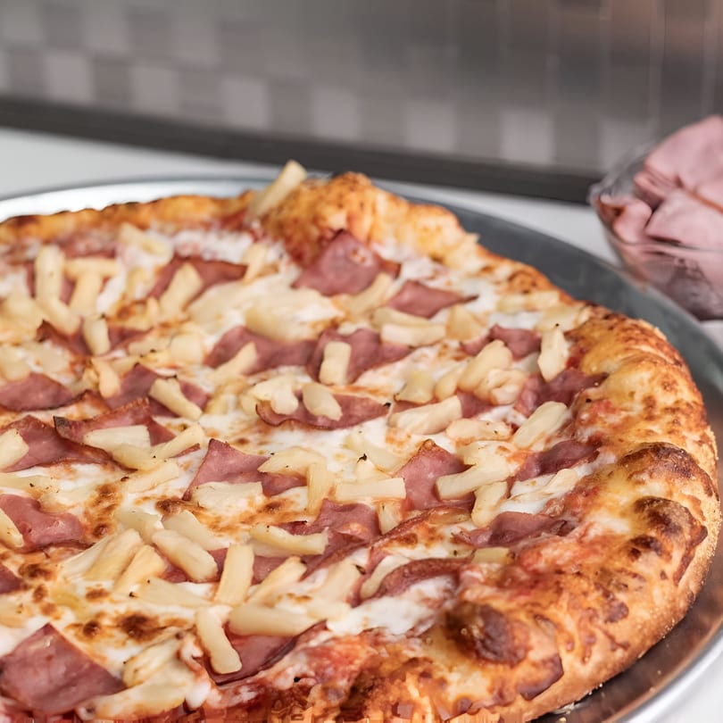 A Big R's Pizza and Wings Hawaiian pizza with ham and pineapple on a metal tray.